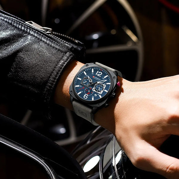 Person wearing a black wristwatch with a blue face in front of a car wheel.
